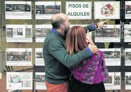 Una pareja observa los anuncios de pisos en alquiler de una inmobiliaria.