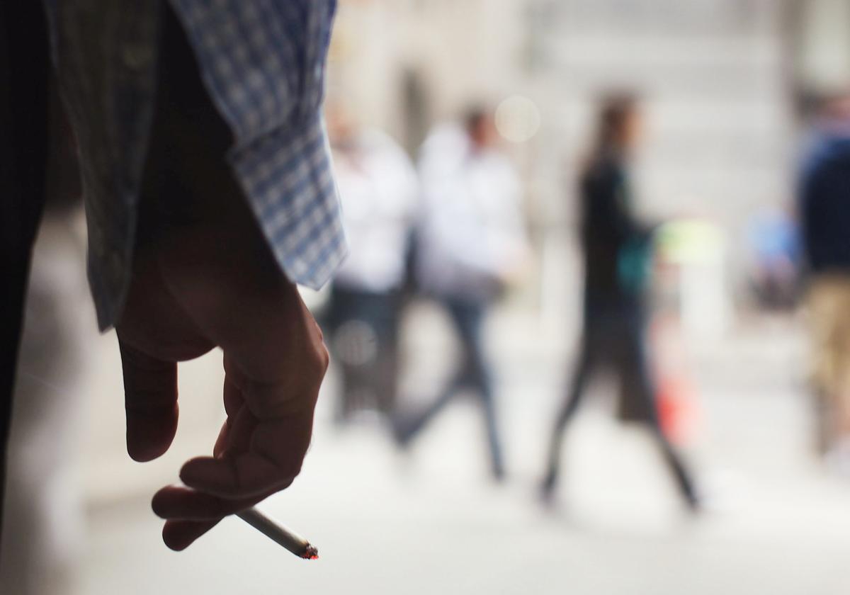 Hombre fuma un cigarrillo en la entrada de un edificio.