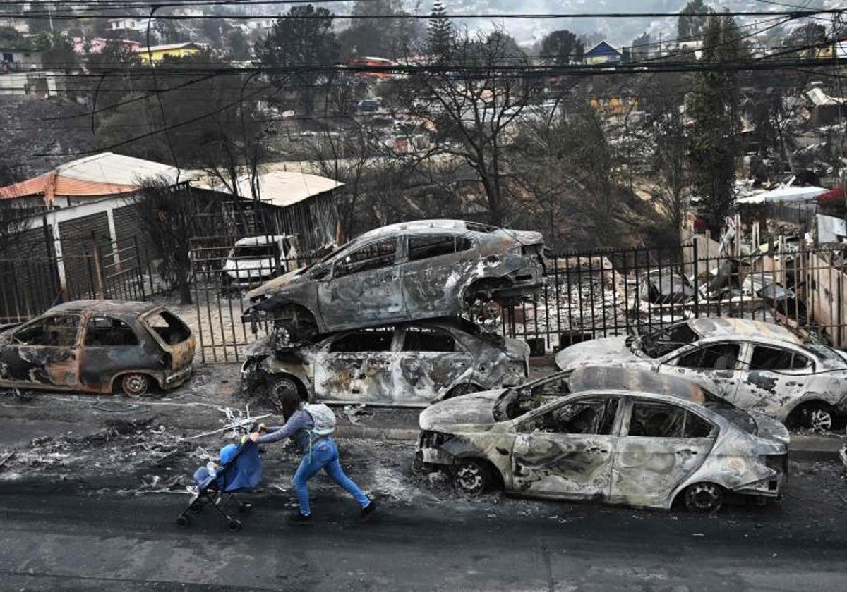 Una mujer con su bebé pasa junto a vehículos quemados por los incendios forestales en la ciudad chilena de Viña del Mar.