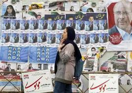 Una mujer iraní camina por una calle de Teherán en la que se exhiben carteles electorales de candidatos.