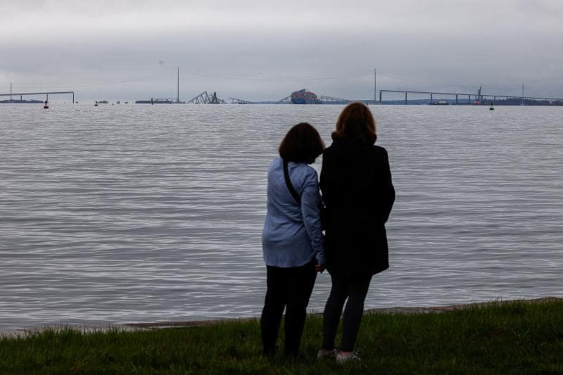Dus mujeres de Baltimore observan desde la distancia los restos del viaducto y el mercante varado.