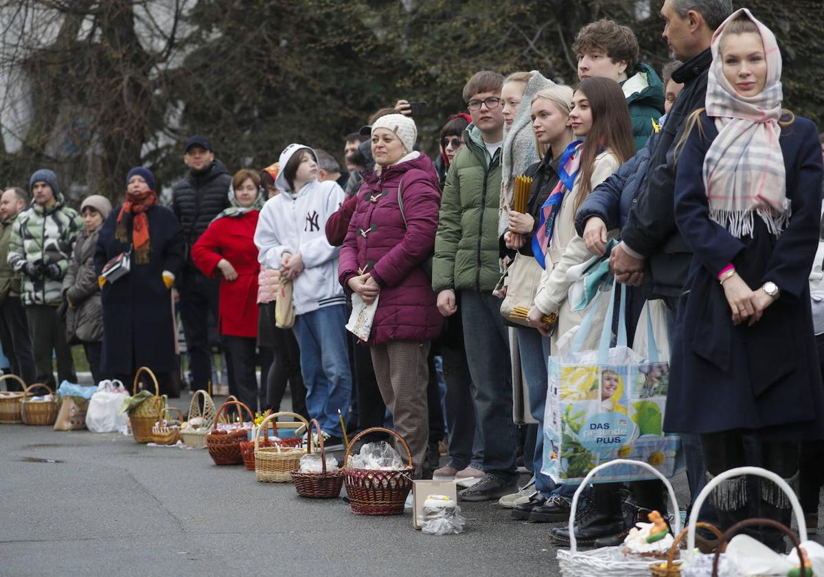 Imagen principal - Ucranianos hacen cola con sus cestas a la espera de ser bendecidas mientras otros creyentes colocan velas en una iglesia de la capital. 