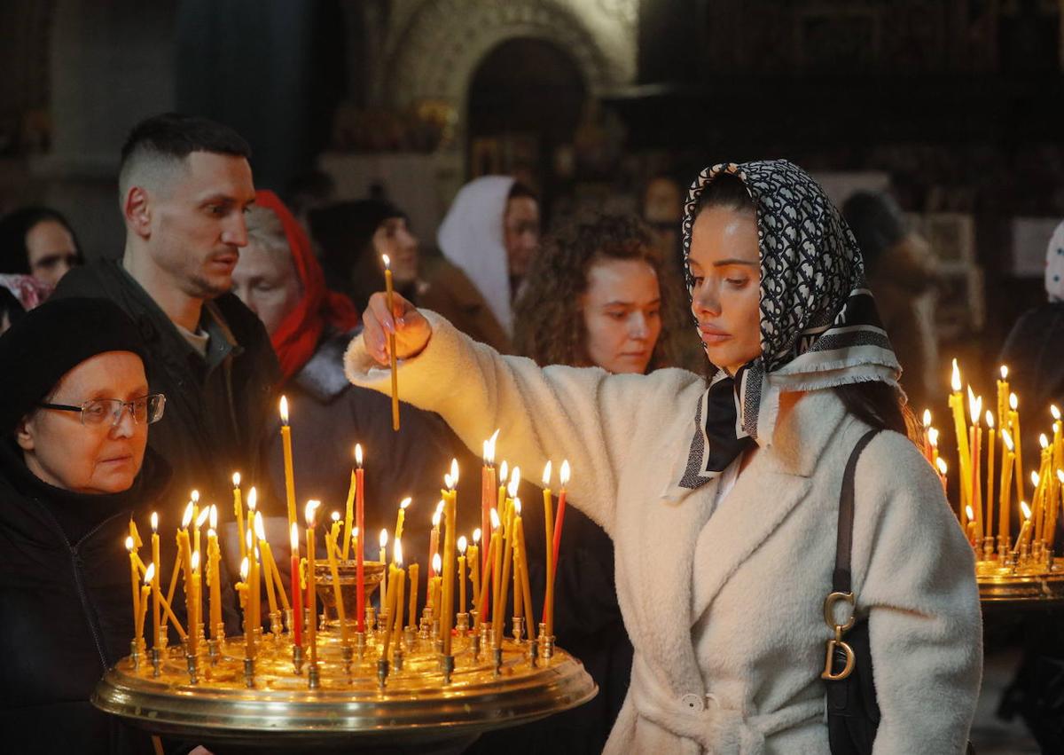 Imagen secundaria 1 - Ucranianos hacen cola con sus cestas a la espera de ser bendecidas mientras otros creyentes colocan velas en una iglesia de la capital. 