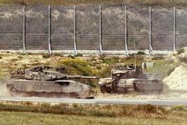 Dos tanques israelíes avanzan hacia una valla fronteriza.