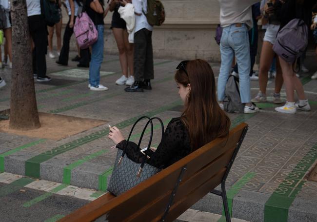 Una mujer fuma sentada en un banco a la salida del colegio en Barcelona.