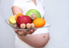 Mujer embarazada muestra un plato con frutas.