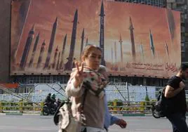 Una iraní hace la señal de la victoria mientras pasa frente a un cartel que arremete contra Israel en las calles de Teherán.