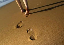 Mujer camina por la arena húmeda de la playa.