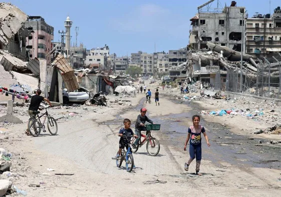 Niños a pie y en bicicleta entre los escombros de Ciudad de Gaza.