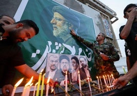 Un grupo de ciudadanos coloca velas y flores junto a retratos del fallecido presidente iraní, Ebrahim Raisi.