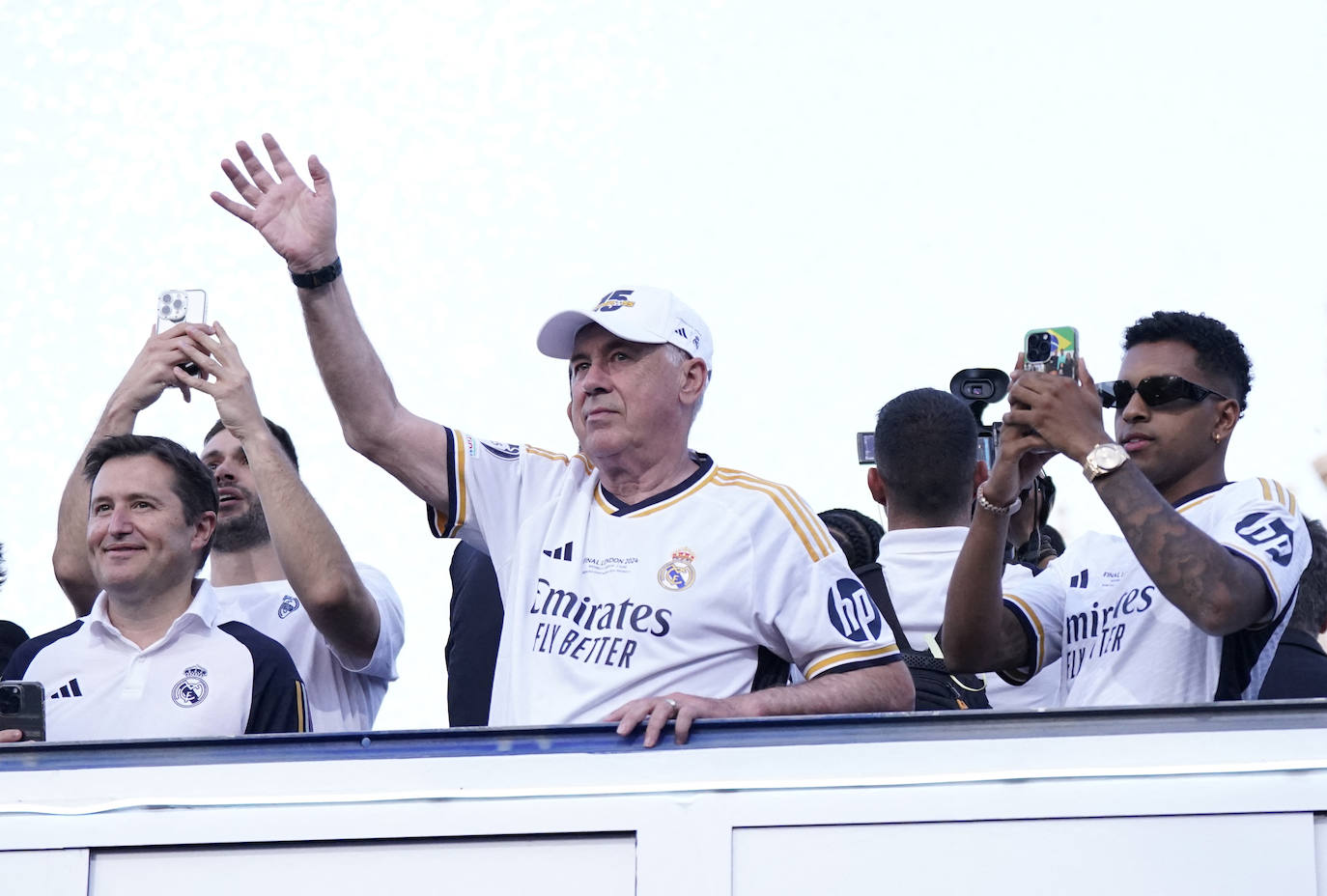 Carlo Ancelotti saluda a los aficionados del Real Madrid que se dieron cita en la Plaza de Cibeles, mientras Rodrygo inmortaliza el momento con su móvil.