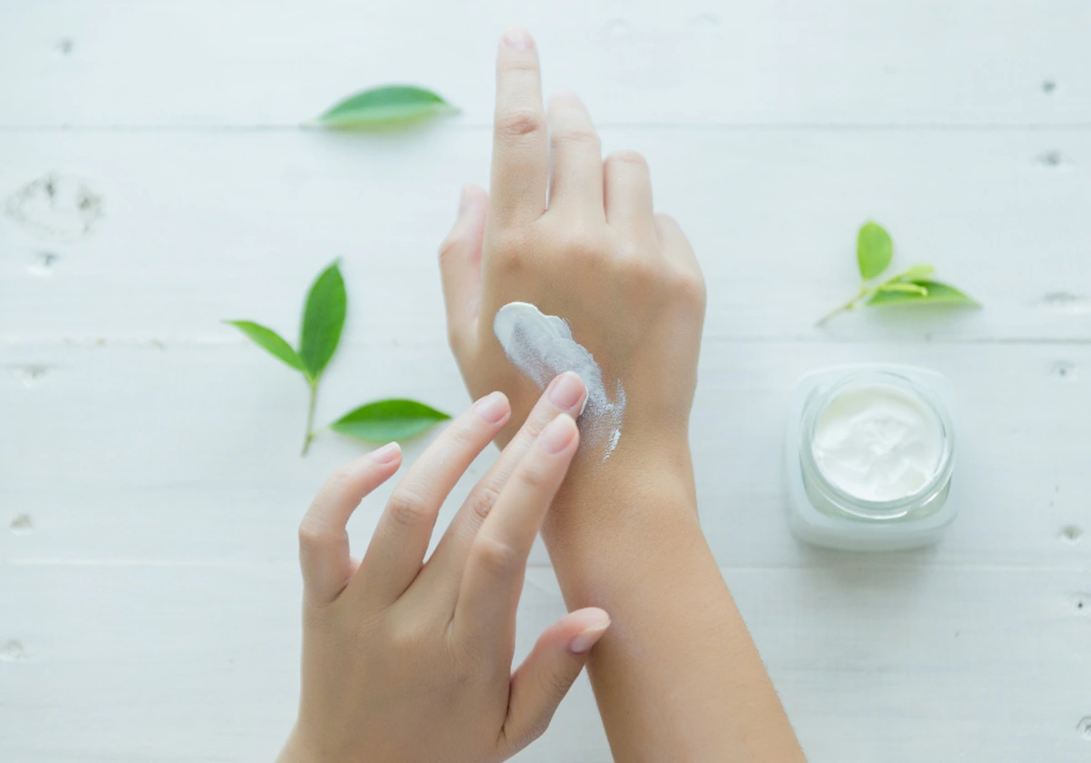 Mujer se echa sobre las manos una crema cosmética y el bote al fondo