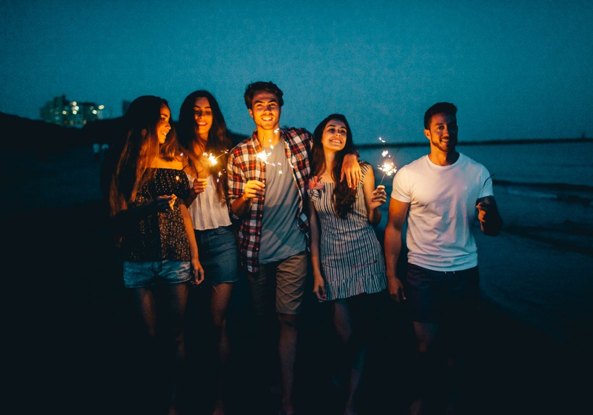 Amigos jóvenes con bengalas en una playa de noche