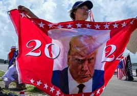 Una mujer porta una bandera con la icónica imagen de Trump en su ficha policial.