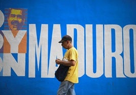 Un hombre pasa junto a un mural de campaña del presidente Nicolás Maduro en Caracas.