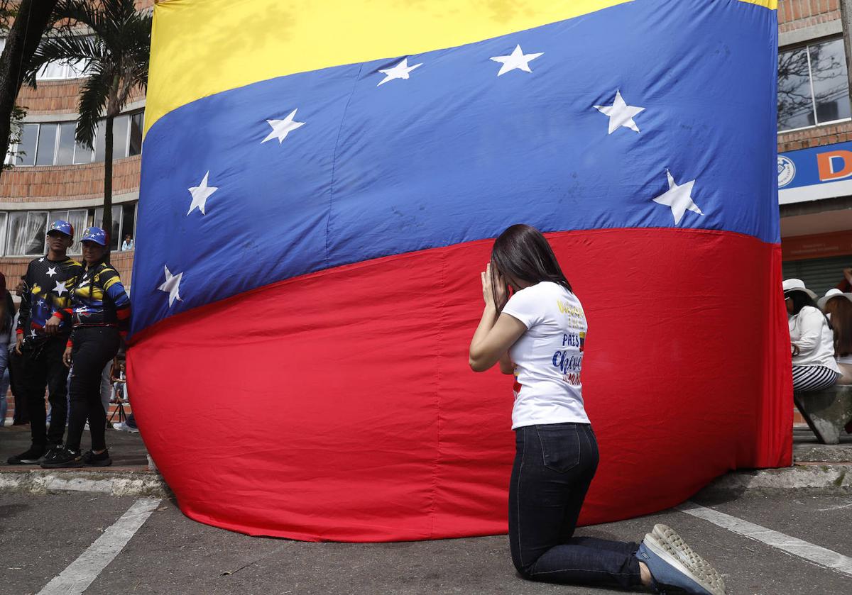 Una mujer reza delante de una bandera venezolana.