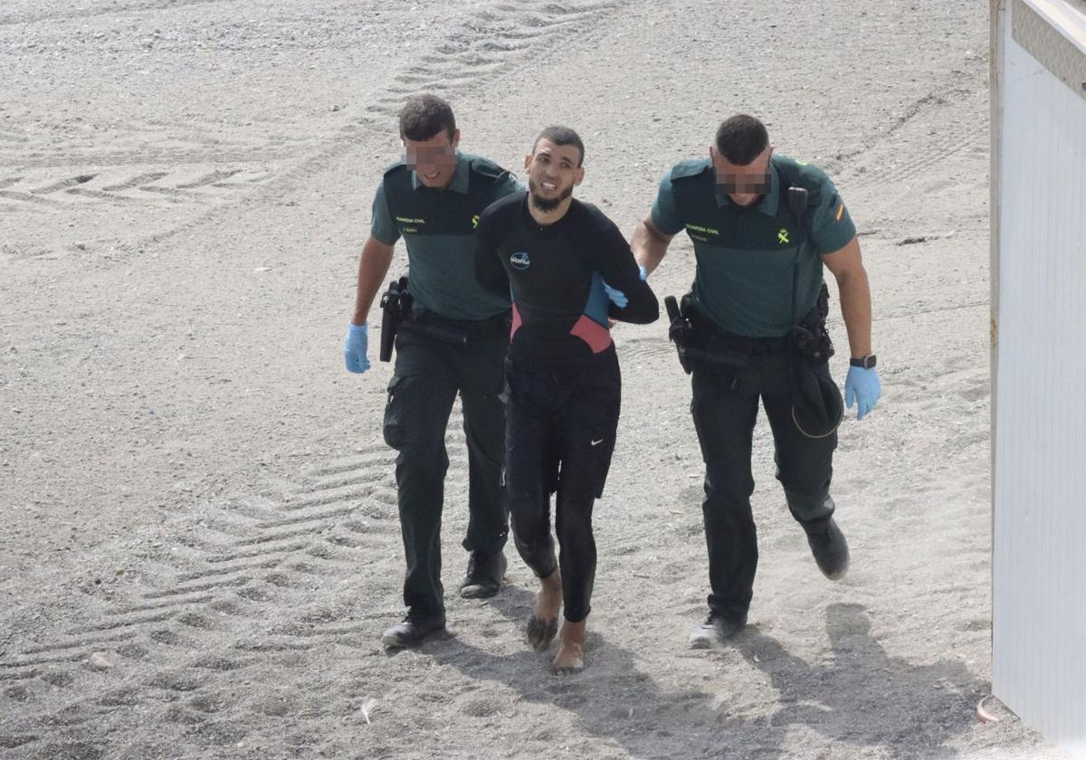 Guardias civiles conducen a un joven que llegó a nado a la playa de El Tarajal.