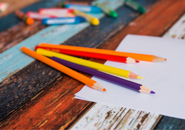 Lápices colorido sobre hojas en blanco en mesa coloreada con ceras al fondo