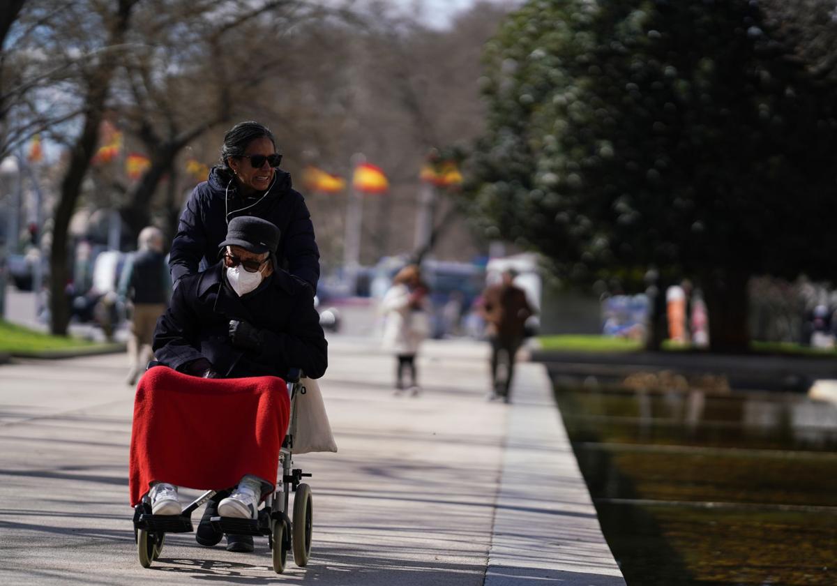 Una mujer con su marido en silla de ruedas por un parque.