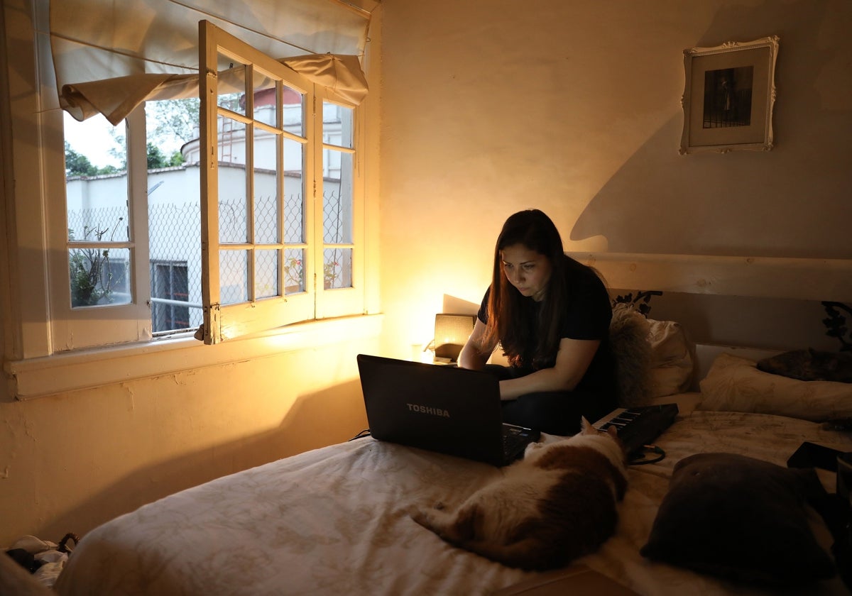 Una chica navega en su ordenador sola en su habitación.