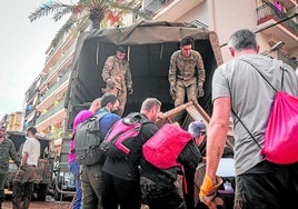 Un grupo de voluntarios ayuda a varios militares a cargar en un camión enseres y muebles en la localidad de Paiporta, de las más afectadas por la DANA.