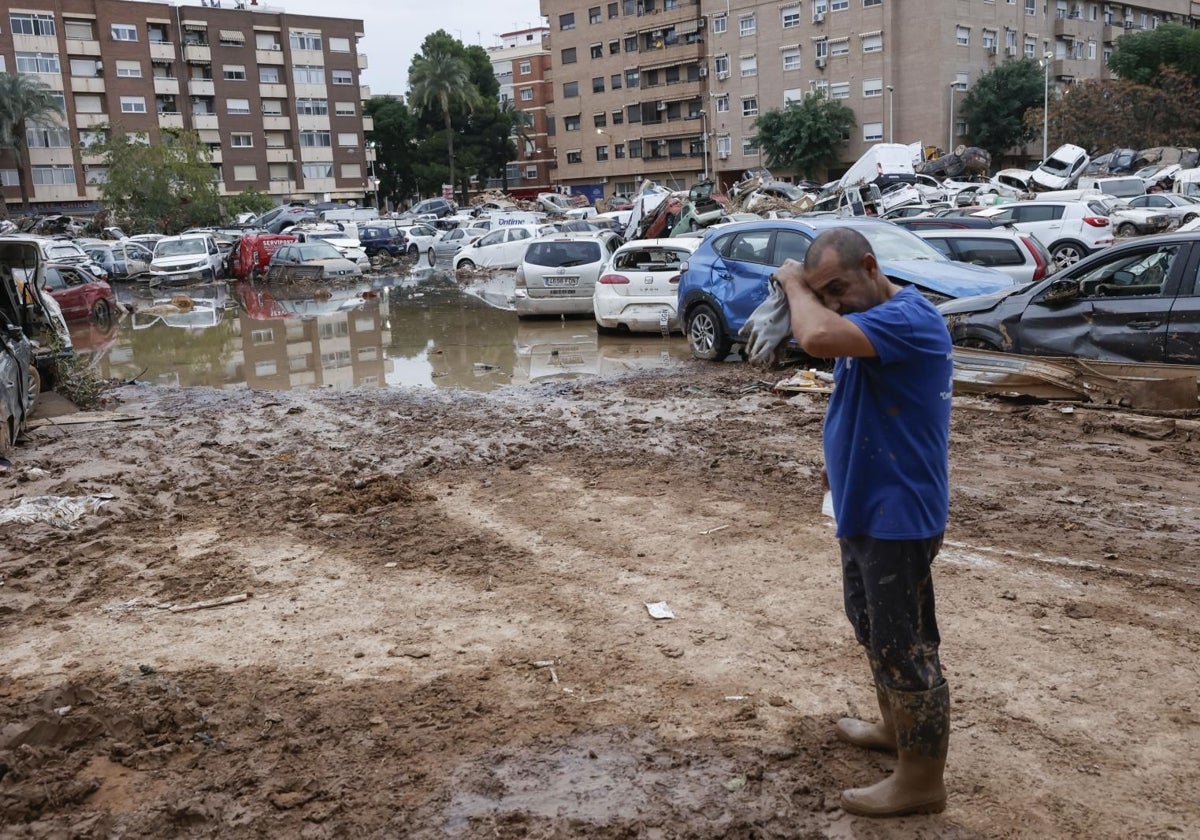 Un hombre junto a varios coches, arrastrados por el agua tras el paso de la dana, en Paiporta