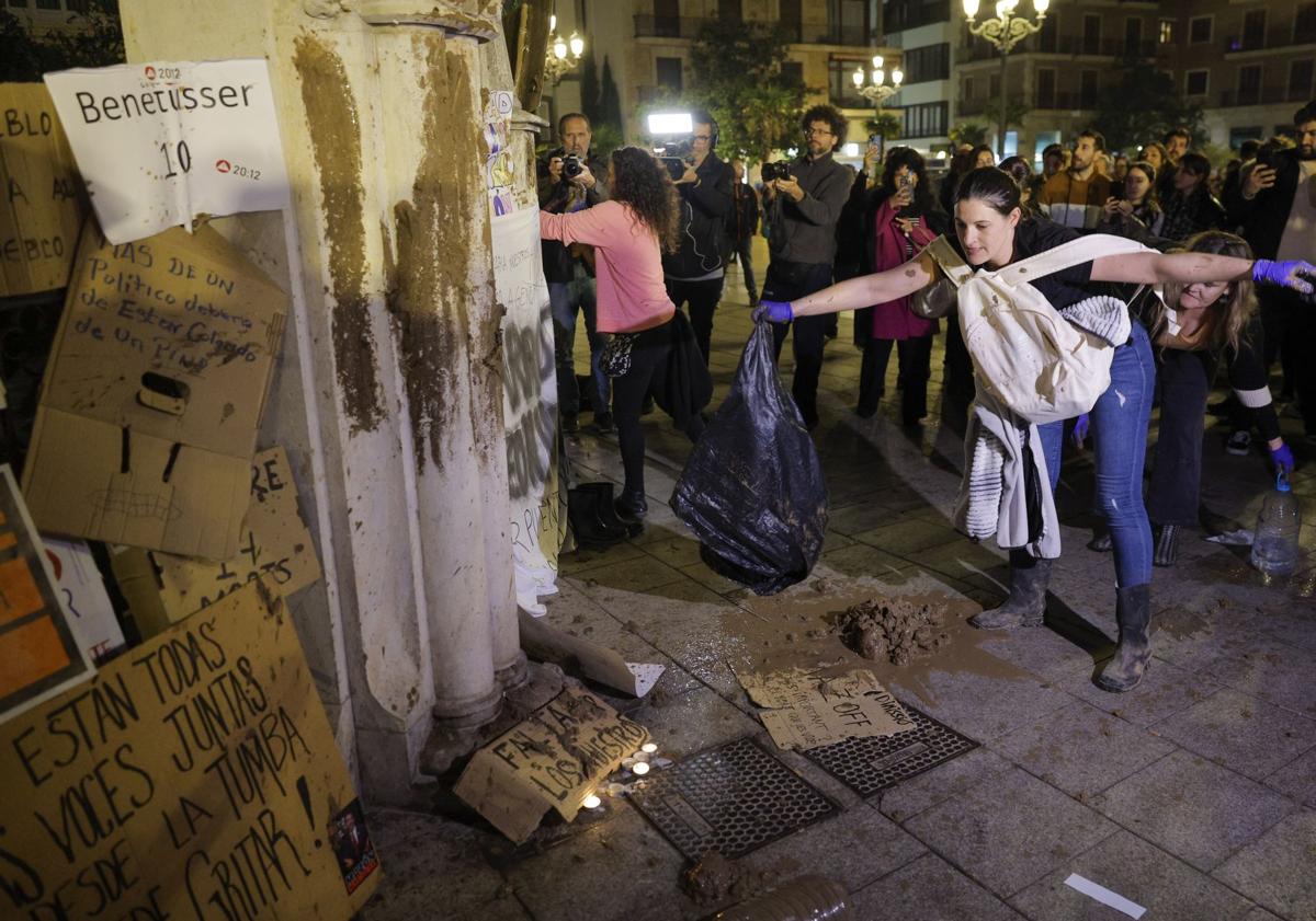 Imagen principal - En la imagen superior, varios manifestantes lanzan barro antes las puertas de un edificio oficial, debajo una pancarta criticando la tardanza en los avisos de la Generalitat por la DANA y, por última, una mujer no puede resistir emocionarse durante la protesta.