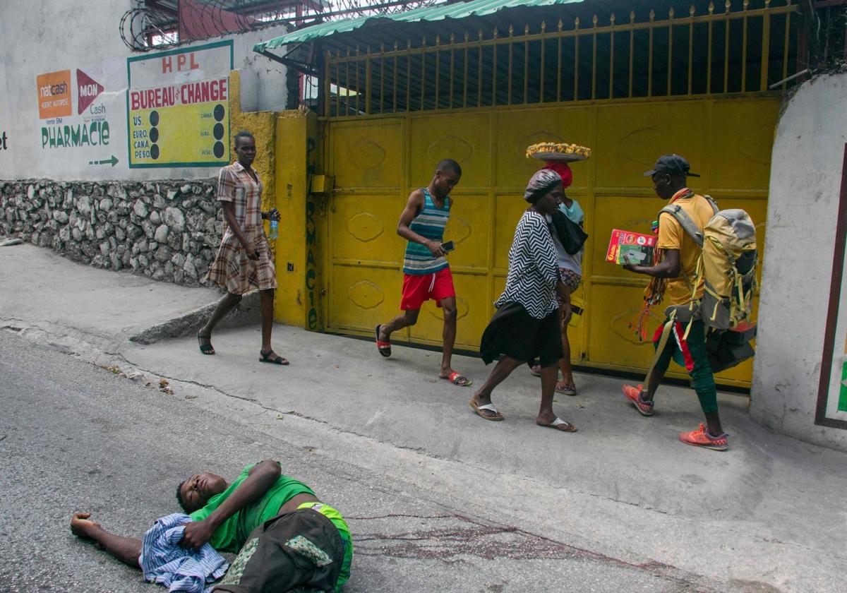 Haitianos caminando frente a un cadáver en una calle de Puerto Príncipe.