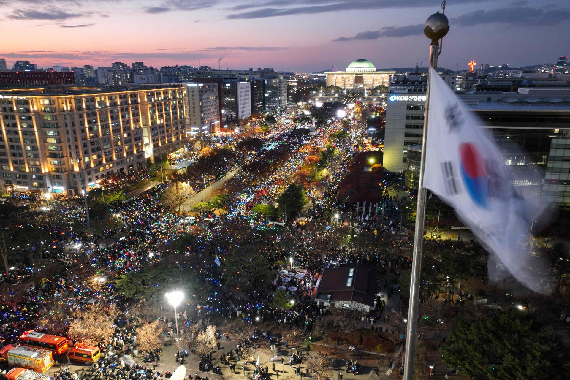 Una bandera de Corea del Sur ondea mientras una marea de personas protesta en contra del presidente de Corea del Sur, Yoon Suk Yeol, frente a la Asamblea Nacional en Seúl.