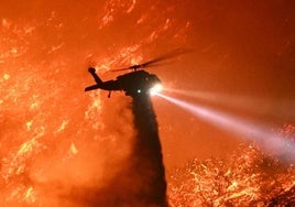 Un helicóptero de extinción arroja agua a un monte en llamas en Los Ángeles.