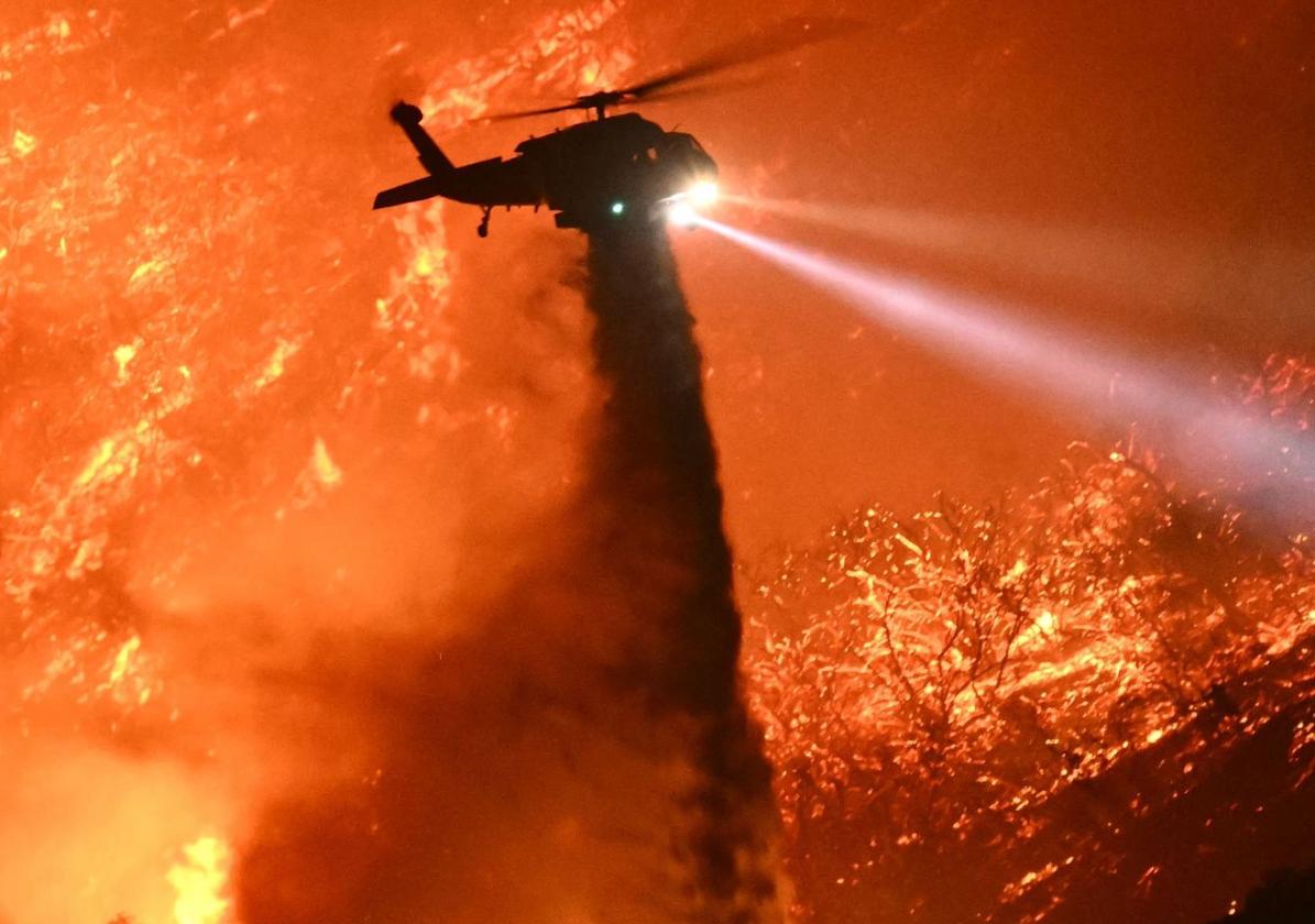 Un helicóptero de extinción arroja agua a un monte en llamas.