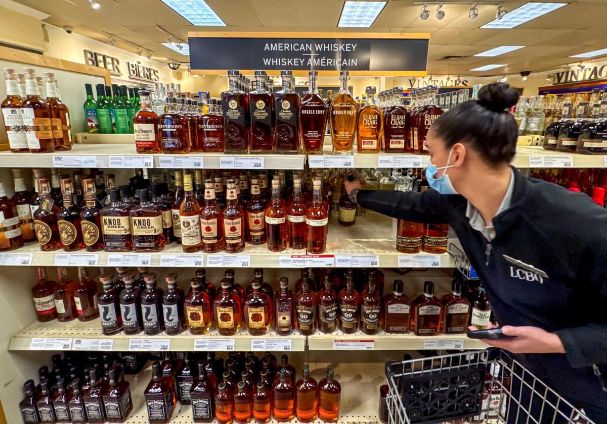 Una empleada de un supermercado canadiense coge botellas de whisky estadounidense, al que Canadá aplicará aranceles.