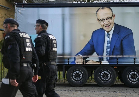 Dos policías alemanes pasan junto a un camión con un cartel de campaña del candidato conservador a la Cancillería, Friedrich Merz.