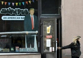 Una mujer camina junto al escaparate de un bar en San Petersburgo en el que se exhibe un retrato de Donald Trump.