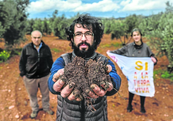 El agricultor Ángel Delgado, con un puñado de tierra del Campo de Montiel, donde una minera busca neodimio. Tras él, Raquel Pérez, portavoz de la plataforma Sí a la Tierra Viva, y Miguel Fuentes, ambos también agricultores.