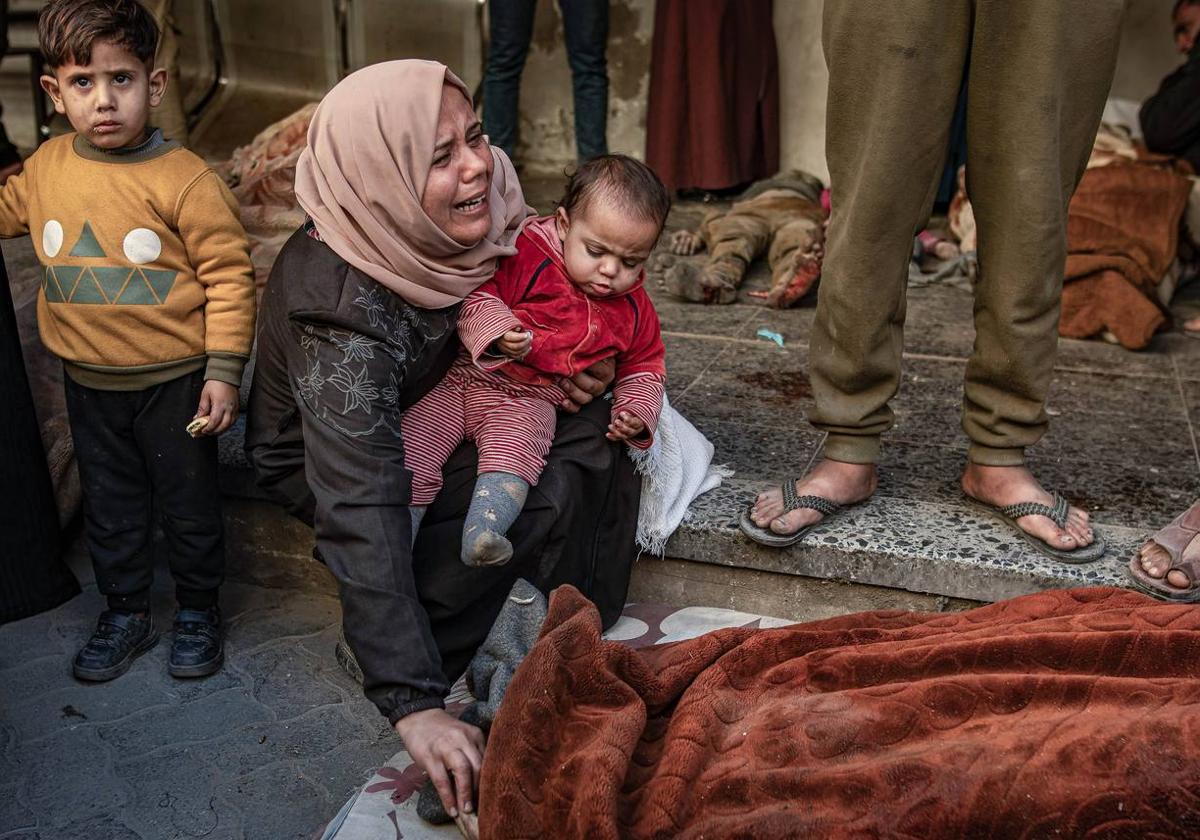 Una mujer, con su bebé en brazos, llora junta al cadáver de una de las víctimas de los ataques de Israel contra un hospital de Gaza.