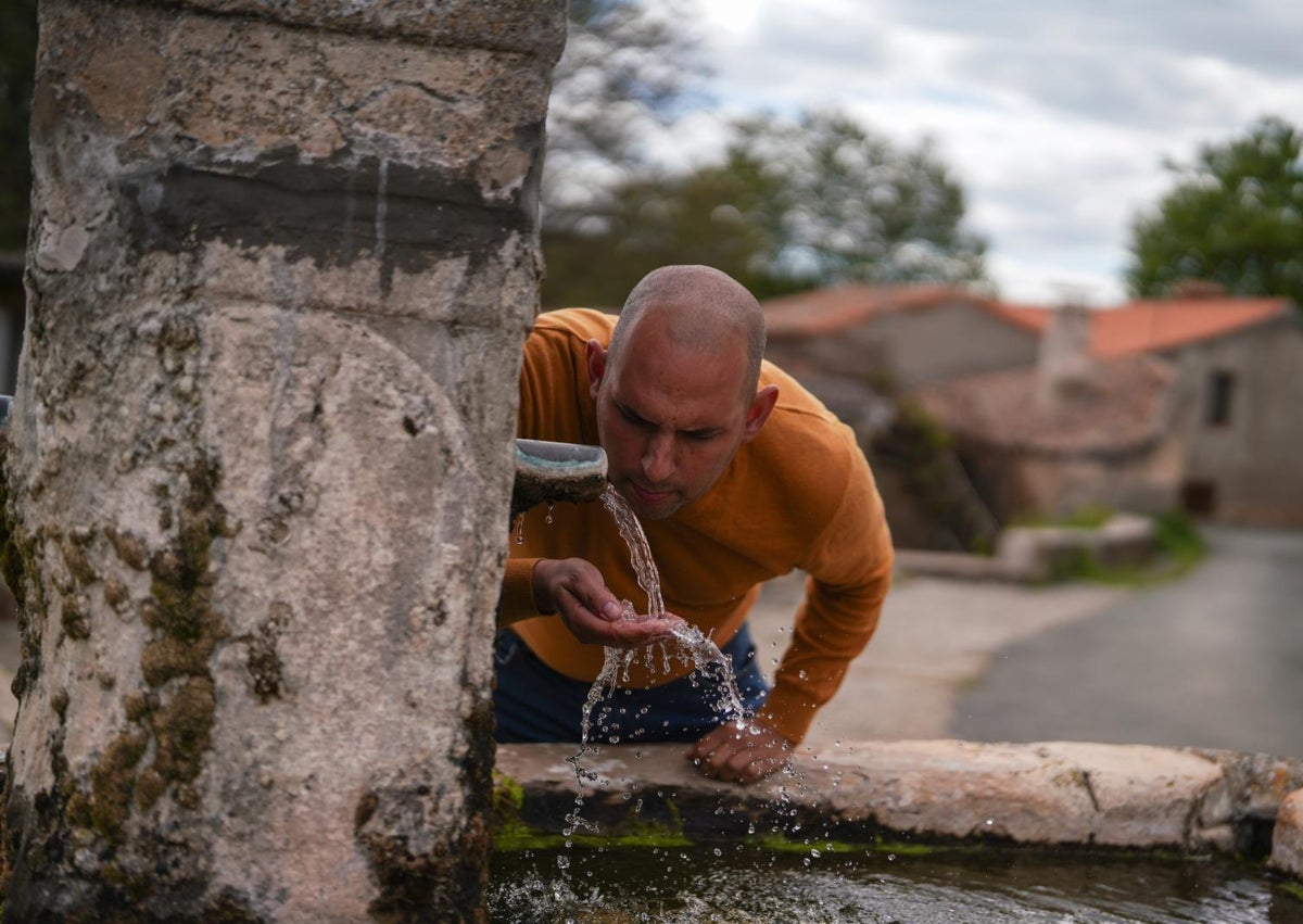 Imagen secundaria 1 - De arriba abajo, Fernando delante de su casa de piedra, que construyeron sus tatarabuelos; bebiendo agua en la fuente de la plaza de Benamira; y en el local social del pueblo donde hay un futbolín.