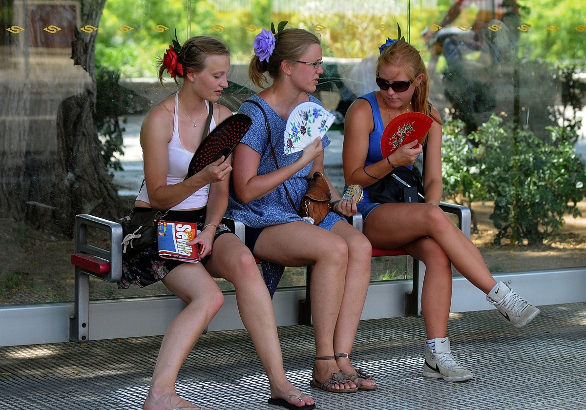 Tres turistas tratan de aliviar la alta temperatura abanicándose en un banco a la sombra.
