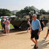 Ciudadanos pasean junto a un vehículo aparcado a la espera del desfile militar.
