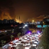 La Policía dirige a los coches hacia una salida de la capital con unos depósitos de combustible ardiendo al fondo.