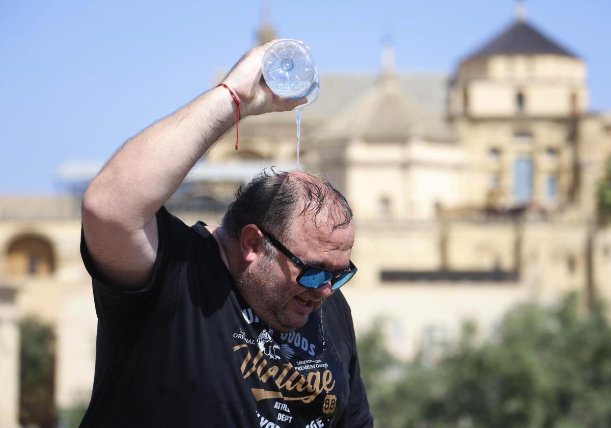 Un hombre se refresca con agua de una botella mientras camina por el Puente Romano de Córdoba
