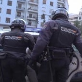 Dos policías sacan al violador del portal de un coche patrulla.