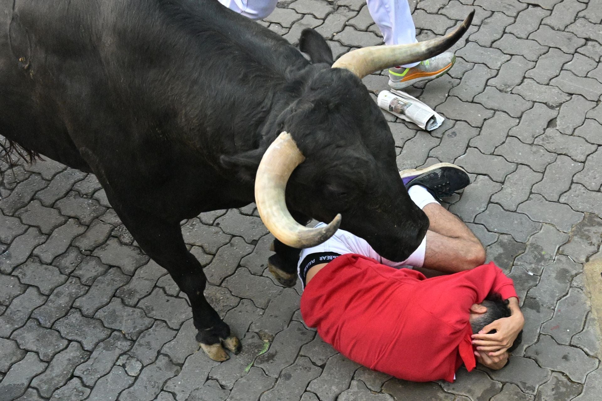 Uno de los mozos se protege la cabeza tras caer al paso de uno de los toros de la ganadería Victoriano del Río Cortés durante el cuarto encierro de los Sanfermines.