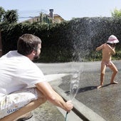 Un padre rocía agua con una manguera a su hija para refrescarla por las altas temperaturas.