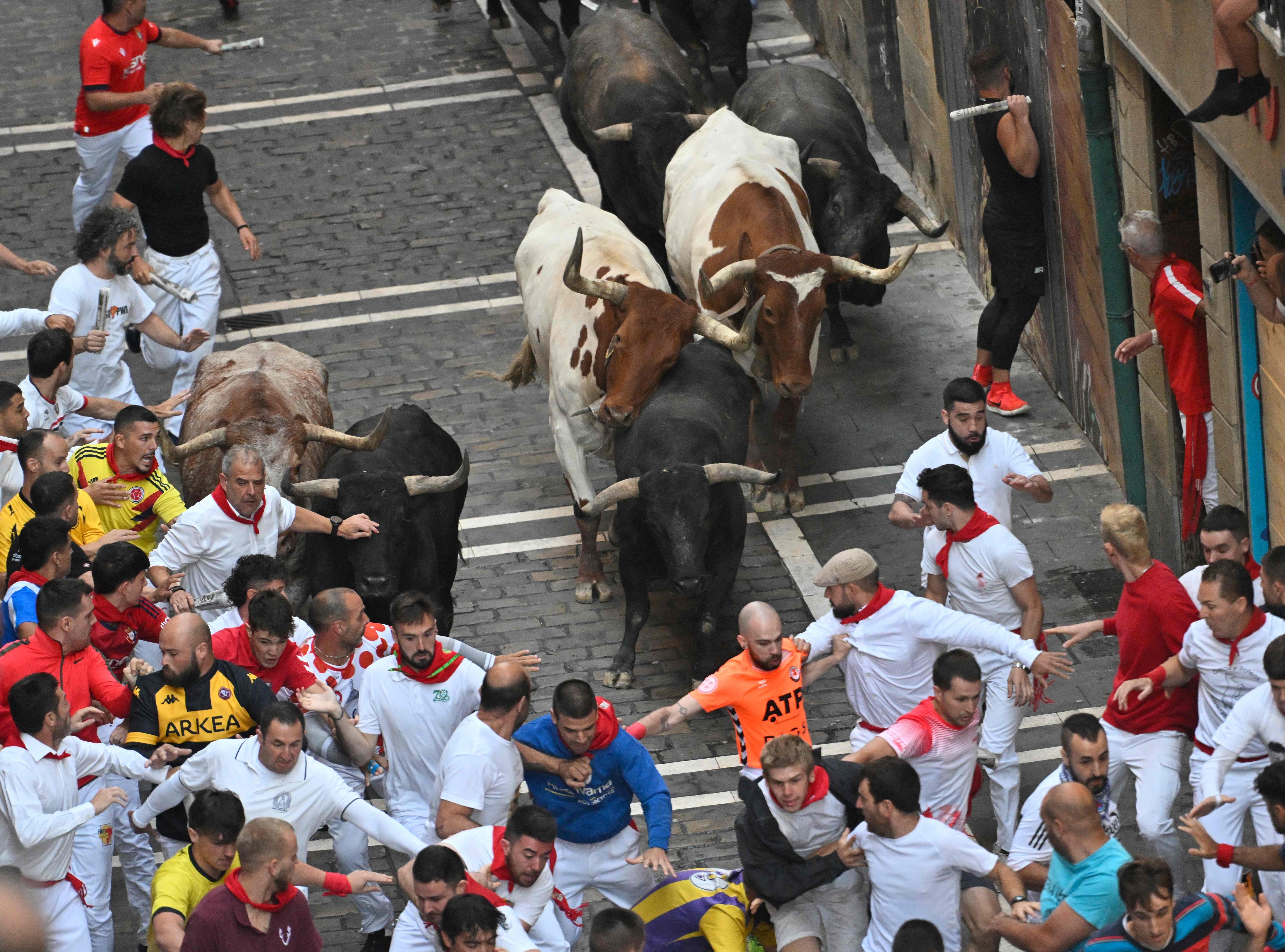 Varios corredores miran a los toros mientras estos les persiguen.