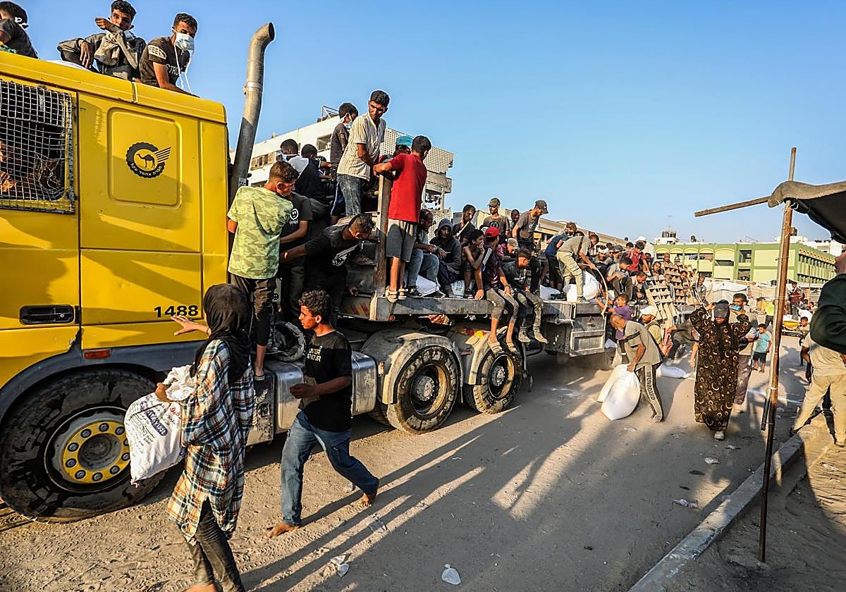 Palestinos con sacos de harina caminan por una calle del sur de Gaza tras acceder camiones con ayuda a través del paso fronterizo de Kerem Shalom.