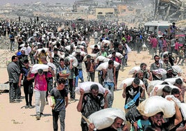Ciudados de Gaza cargan a hombros con sacos de comida en un centro de reparto.