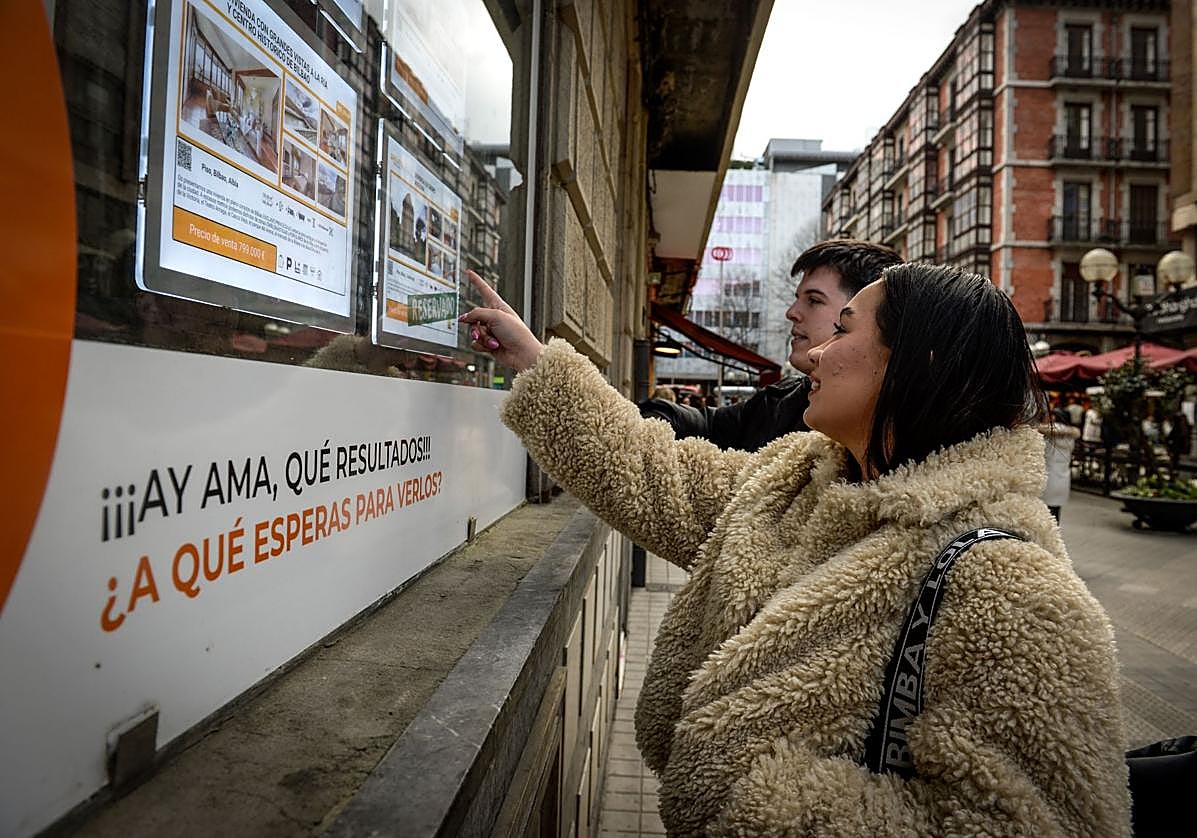Dos jóvenes mirando anuncios de viviendas que se venden o alquilan.