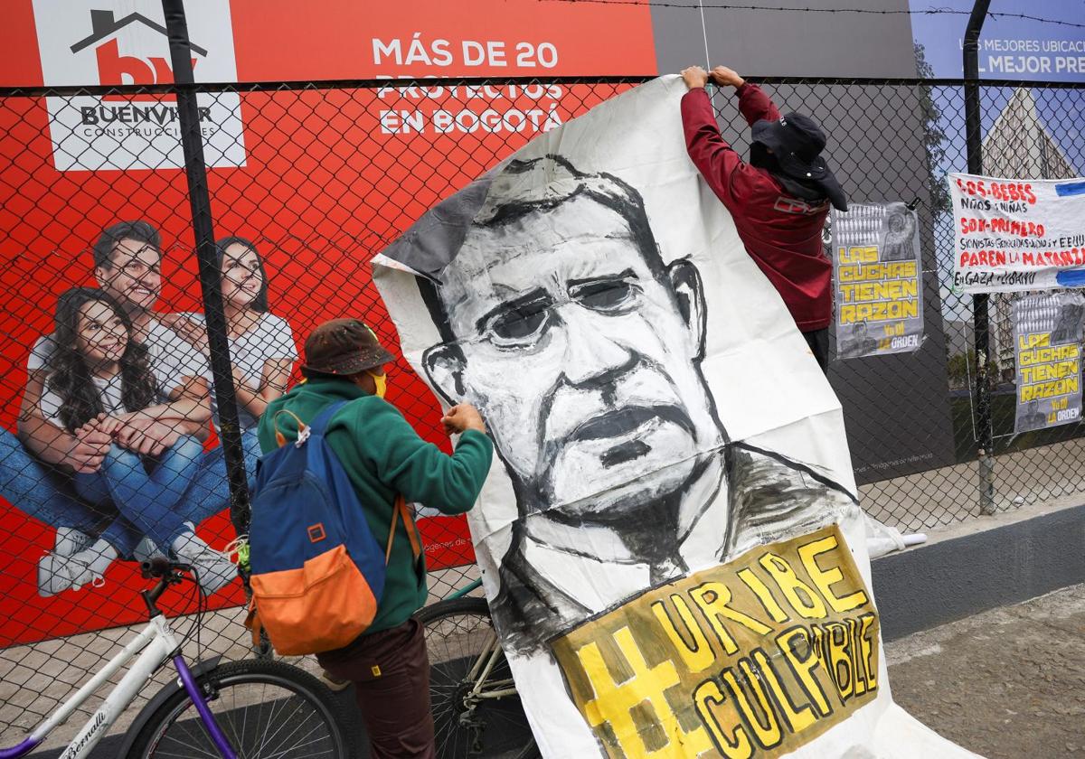 Dos manifestantes cuelgan en Bogotá una pancarta para protestar contra el expresidente colombiano Álvaro Uribe.