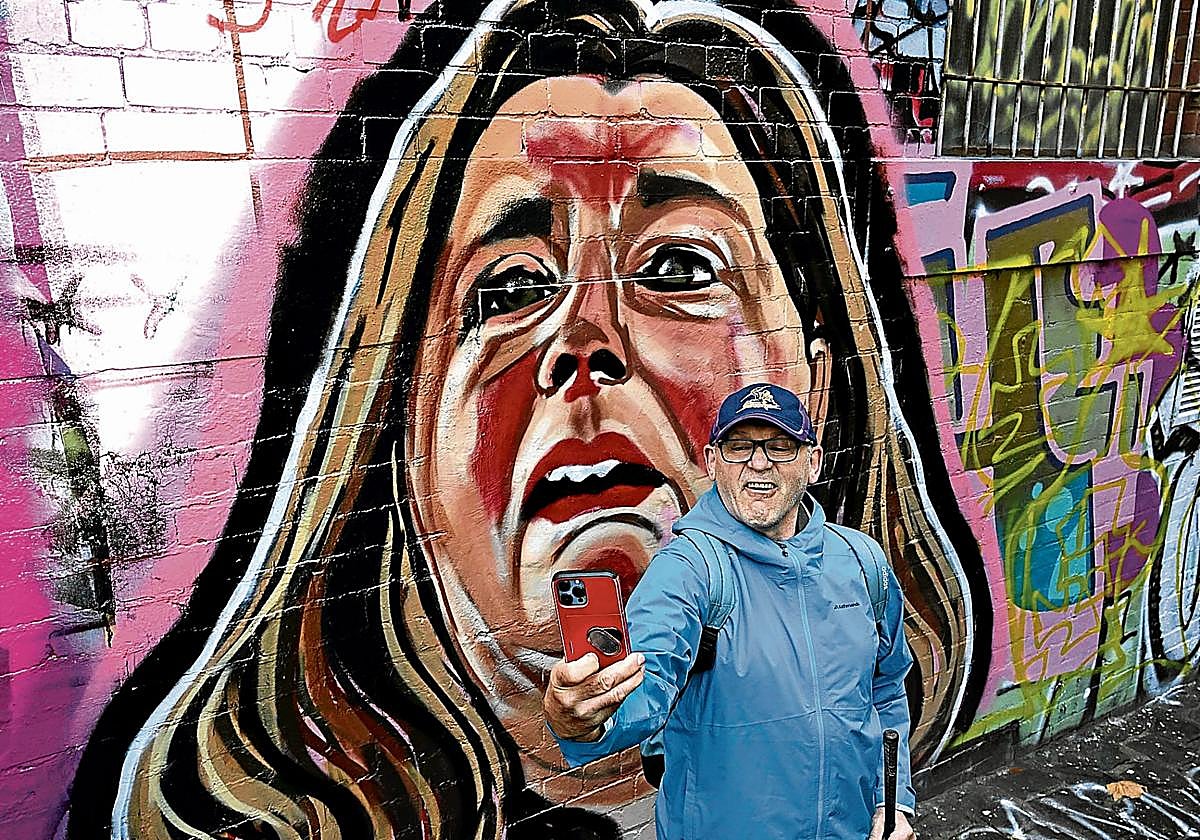 Un hombre se hace un selfi en un callejón de Melbourne delante de un mural sobre Erin Patterson.
